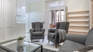 A modern living room with a grey sofa, two armchairs, a glass coffee table, and a dining area in the background. - Dreams of the Cathedral * Oasis in Santa Cruz * (Sevilla)