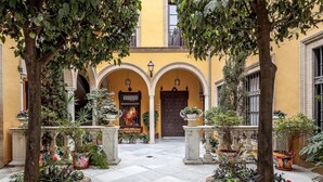 A courtyard with a yellow building, arched doorways, and potted plants. - Dreams of the Cathedral * Oasis in Santa Cruz * (Sevilla)