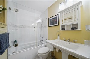 A modern bathroom with a glass-enclosed shower, a white toilet, and a sink with a mirror above it.