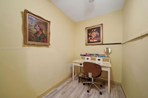 A small room with a desk, chair, and two framed paintings on the walls.