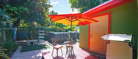 Une terrasse avec un parasol rouge, deux chaises et une petite table.