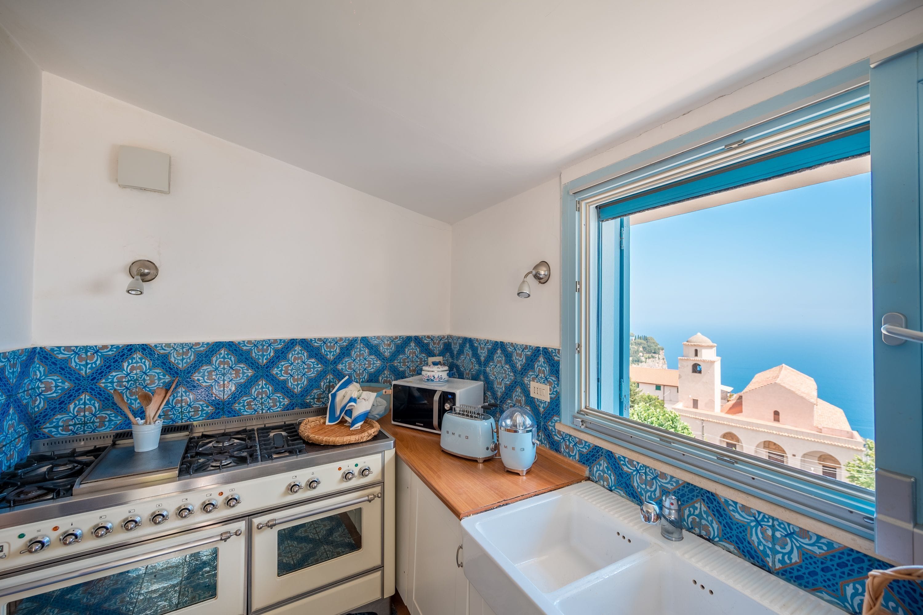 Une cuisine équipée d’une cuisinière, d’un four et offrant une vue sur les immeubles par une fenêtre.