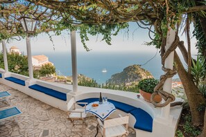 A terrace with a table and chairs, overlooking a coastal view with a boat in the distance. - Villa la Campanella in Ravello (Scala)