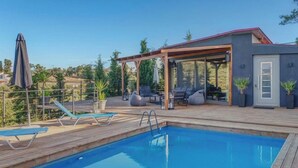 Un espace piscine avec des chaises longues, un coin salon abrité et un bâtiment moderne doté d’un toit rouge.