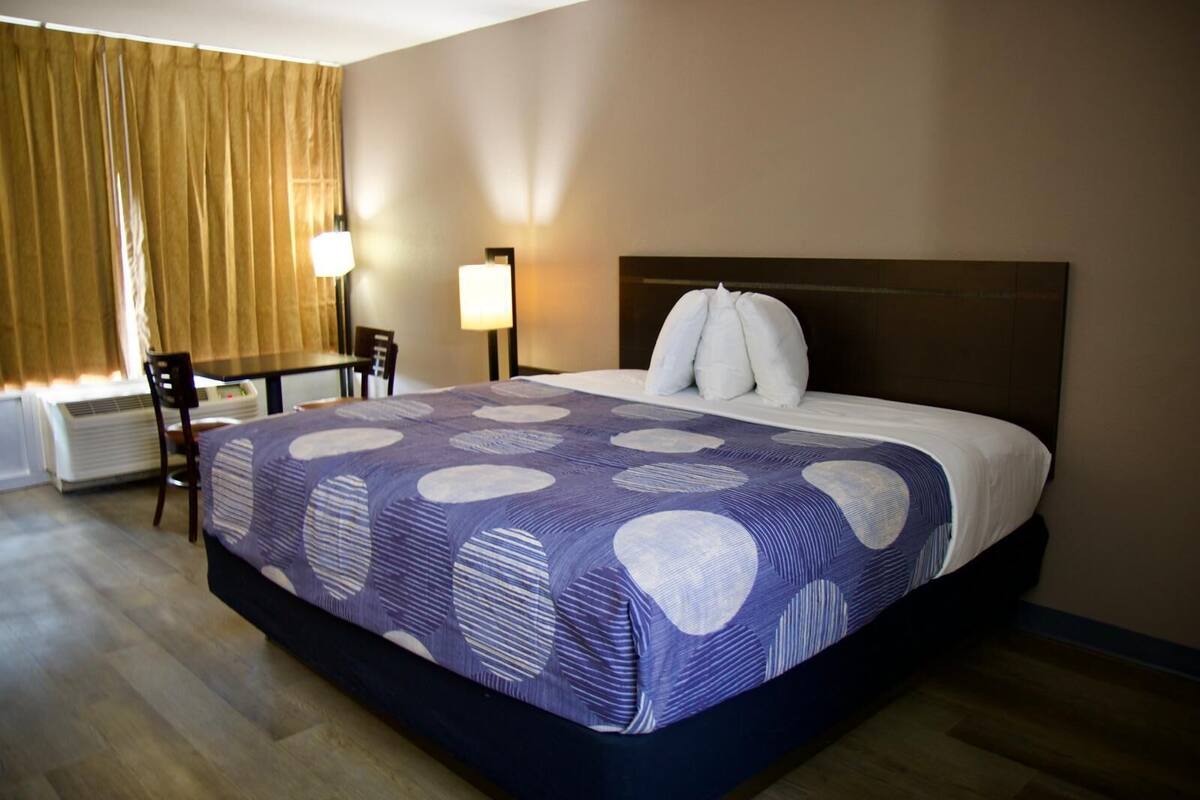 A hotel room with a large bed, two bedside lamps, a wooden chair, and a table.
