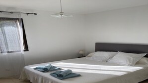 A neatly made bed with white linens and rolled towels, a bedside lamp, and a window with a sheer curtain. - Maison récente avec piscine privée à la campagne. (Urtaca)