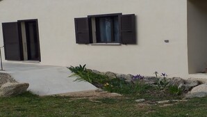 A modern building with two large windows and a door, surrounded by a landscaped garden with rocks and plants. - Maison récente avec piscine privée à la campagne. (Urtaca)