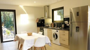 A modern kitchen with a dining table, stainless steel appliances, and a view of greenery outside. - Maison récente avec piscine privée à la campagne. (Urtaca)