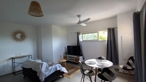 Una stanza con un letto, una TV, una ventola a soffitto, un tavolo da pranzo con sedie e una finestra con tende.