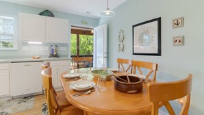 A dining area with a wooden table set for four, white cabinets, and a view of the outdoors. - Dog Friendly w/ Fenced Backyard - Golf Cart Included - Hot Tub - Fire Pit (Oak Island)