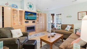 A living room with a fireplace, wooden cabinets, and a television. - Dog Friendly w/ Fenced Backyard - Golf Cart Included - Hot Tub - Fire Pit (Oak Island)