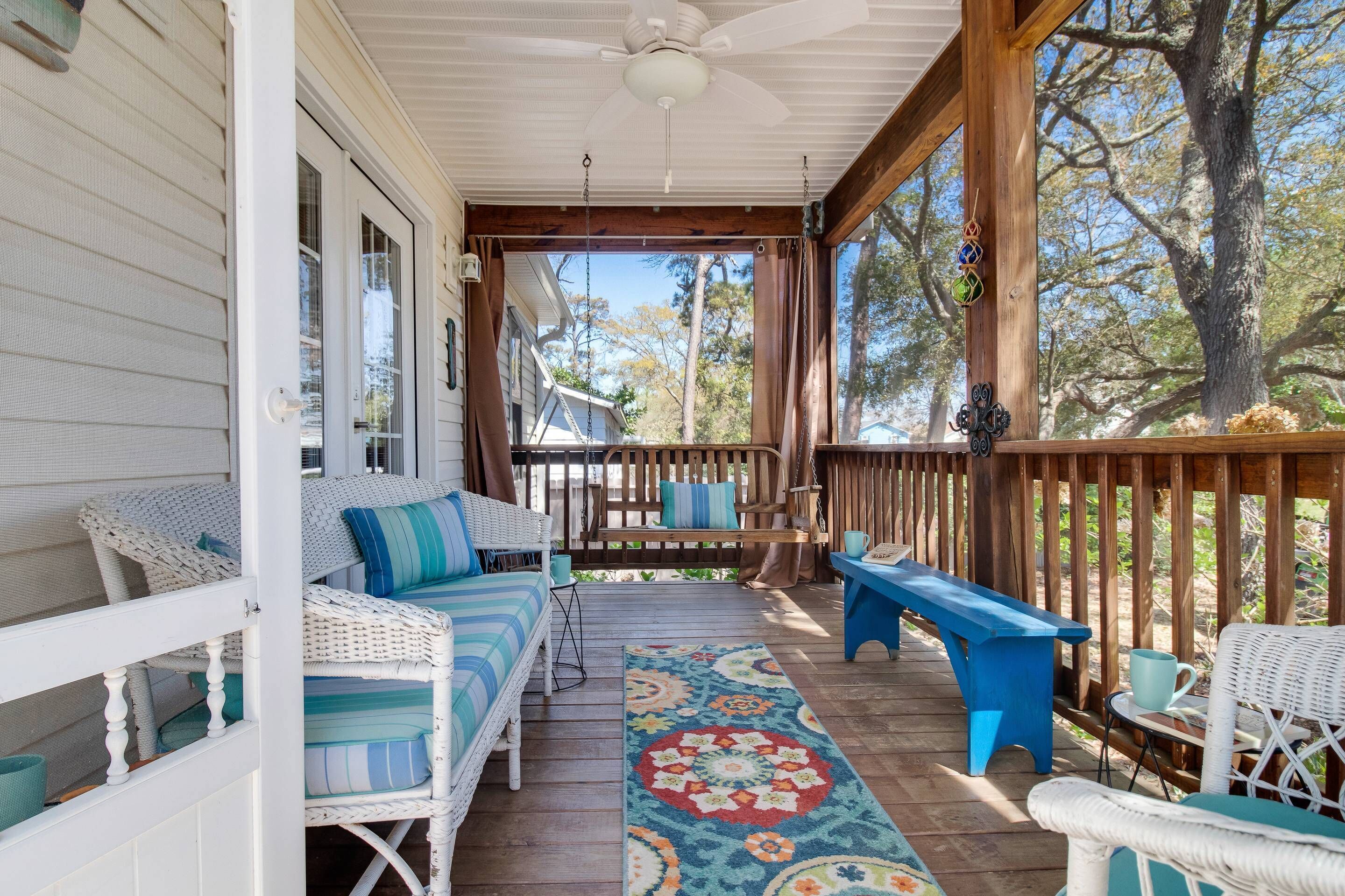 A covered porch with wicker furniture, a colorful rug, and a wooden railing.