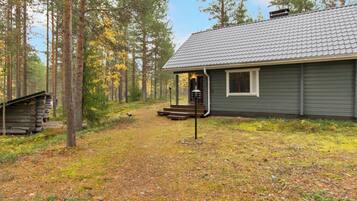 Mökki, jossa on kuisti ja portaat, jotka johtavat sisäänkäynnille. Mökkiä ympäröi metsäalue.