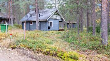 A cabin with a gabled roof, surrounded by dense forest.