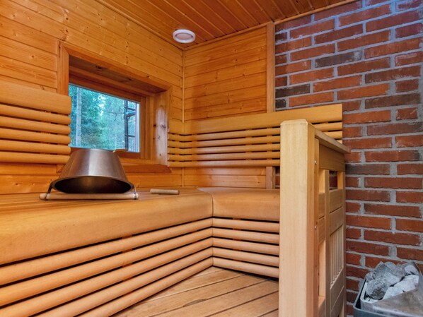A sauna room with wooden walls, a window, and a metal heater.