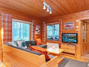 Interior acolhedor de uma cabana com sofá, televisão e janela com vista para uma floresta.