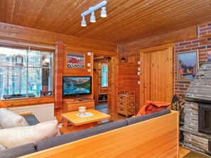 A cozy cabin interior with a wooden interior, a television, a fireplace, and a window overlooking a forest.