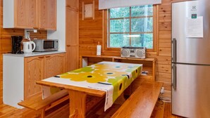 Uma cozinha estilo cabana, com paredes de madeira, uma geladeira de aço inoxidável, um micro-ondas, uma cafeteira e uma mesa com toalha de mesa florida.