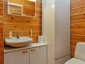 Un baño con pared de madera, un lavabo blanco con dispensador de jabón, un inodoro y un espejo.