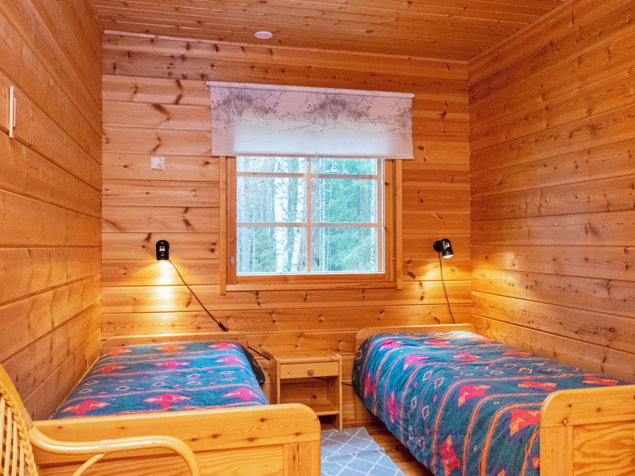 Una cabaña con dos camas de madera, una mesita y un ventanal con vista a árboles.