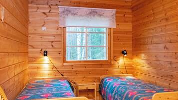 Una cabaña con dos camas de madera, una mesita y un ventanal con vista a árboles.
