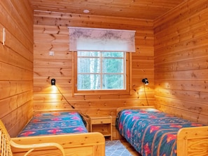 Una cabaña con dos camas de madera, una mesita y un ventanal con vista a árboles.