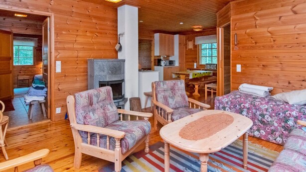 Interior acolhedor de uma cabana, com paredes de madeira, lareira, área de jantar e sala de estar com sofá e poltronas.