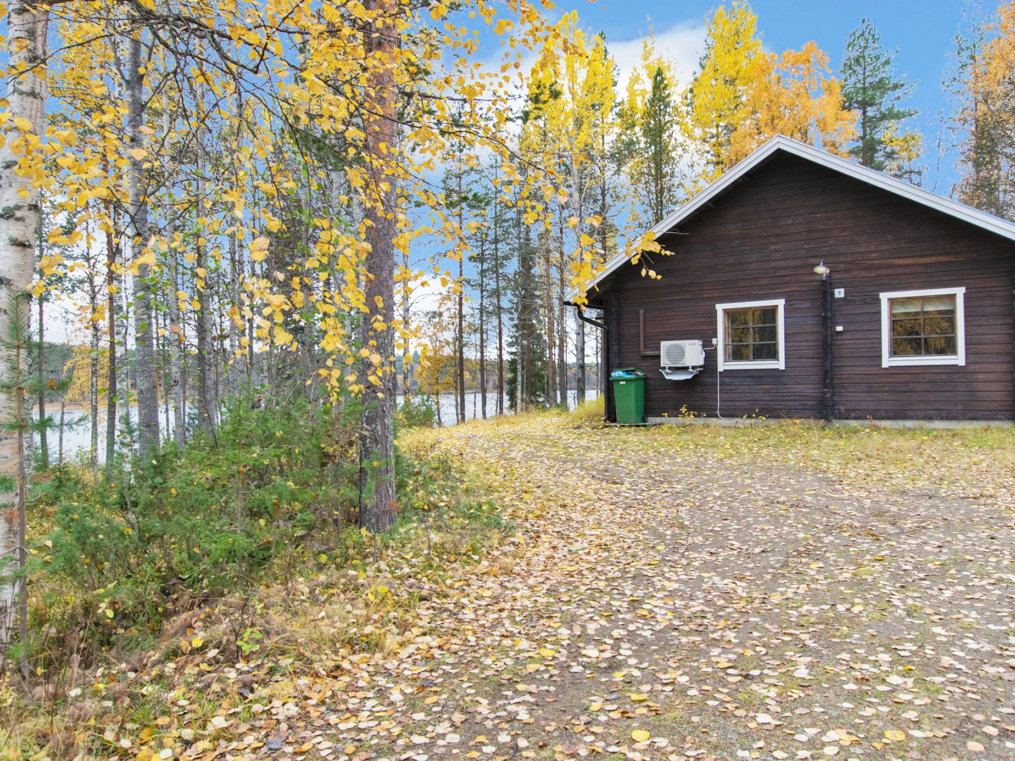A cabin with a clear view of a lake, surrounded by trees with yellow leaves.