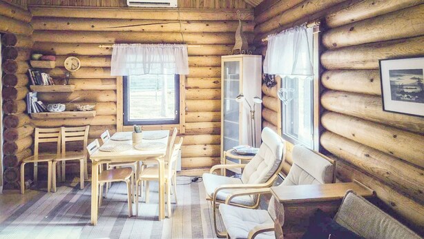 L’intérieur d’une cabane en rondins, avec une table à manger, des chaises, un canapé, une lampe et une horloge au mur.