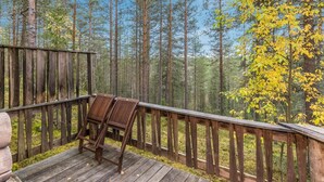 Une terrasse en bois avec une rambarde en métal, donnant sur une forêt où s’élèvent de grands arbres, et où un arbre aux feuilles jaunes se trouve au premier plan.