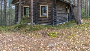 Une cabane en rondins avec deux fenêtres et une cheminée, entourée d’une forêt.