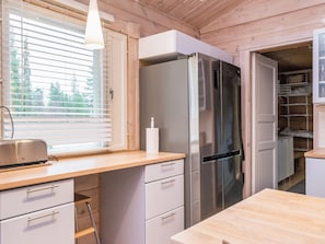 A kitchen with a stainless steel refrigerator, wooden cabinets, a window with blinds, and a countertop with a toaster.