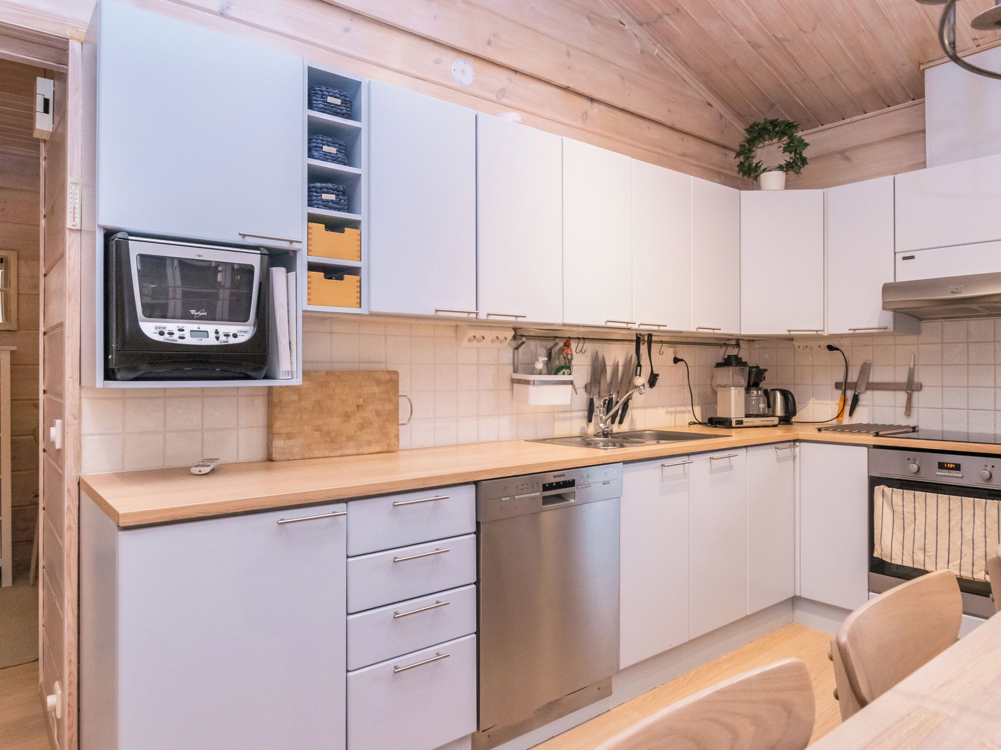 Een moderne keuken met witte kasten, een ingebouwde oven, een vaatwasser en een houten aanrecht.