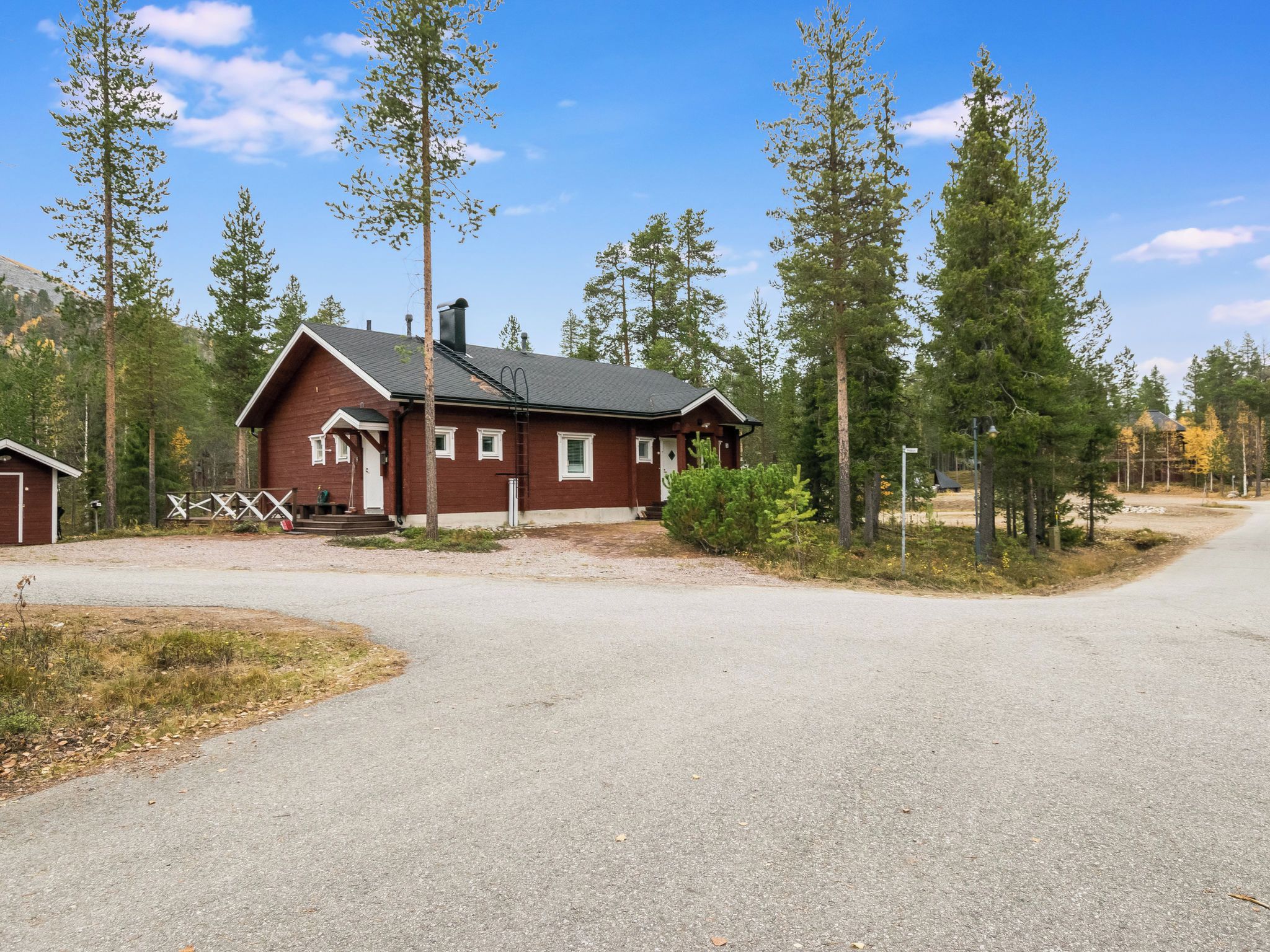 Une cabane à deux étages, dotée d’une cheminée, entourée de grands pins et surplombant un ciel dégagé.