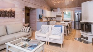 A cozy living room with a sofa, armchairs, and a coffee table. There is a kitchen area with a refrigerator, stove, and dining table. - Isokuru 3 by Interhome (Pelkosenniemi)