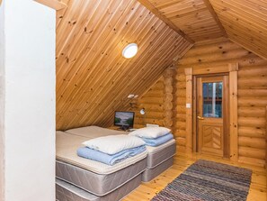 Een slaapkamer in een blokhut met een schuine plafond, een televisie op een standaard, twee bedden met kussens, en een houten deur.