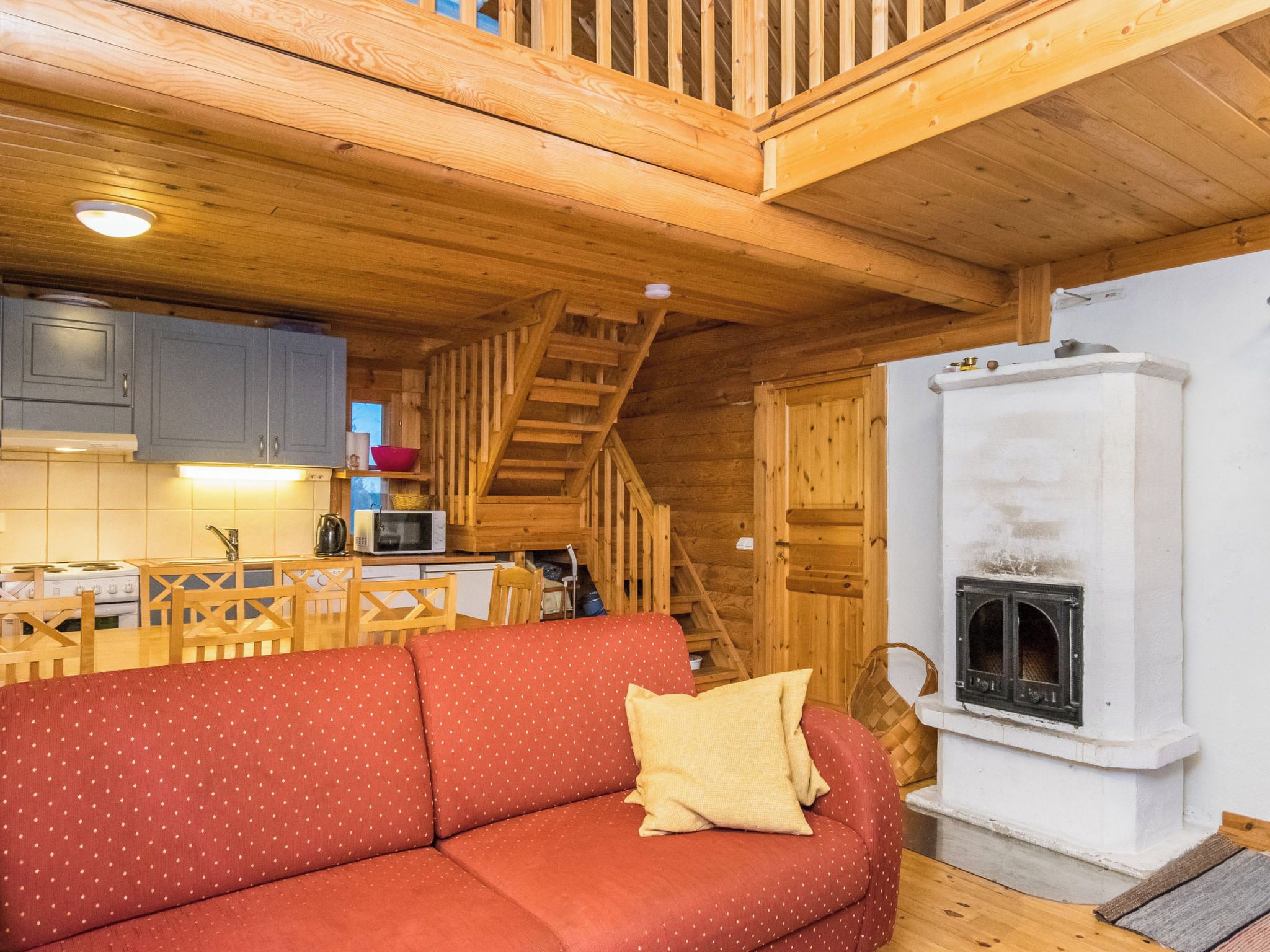 Interior acogedor de una cabaña con escalera de madera, kitchenette, sofá rojo y chimenea.