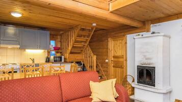 Interior acogedor de una cabaña con escalera de madera, kitchenette, sofá rojo y chimenea.