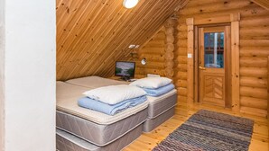 A cozy log cabin bedroom with a sloped ceiling, two beds, a television, and a door. - Kuukkelin tupa 2 by Interhome (Pelkosenniemi)