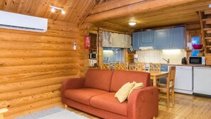 A cozy cabin interior with a wooden interior, a red sofa, a dining table with chairs, and a kitchenette. - Kuukkelin tupa 2 by Interhome (Pelkosenniemi)