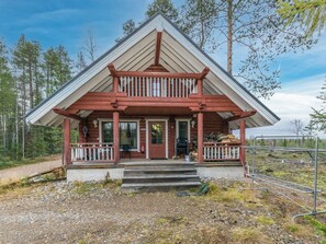 A wooden cabin with a balcony, a front door, and a porch area.