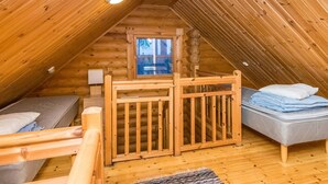 A cozy attic bedroom with a wooden sloped ceiling, a small window, a bed, a bench, and a desk with a lamp. - Kuukkelin tupa 2 by Interhome (Pelkosenniemi)