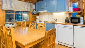A wooden interior with a dining table and chairs, a kitchen with blue cabinets, a microwave, and a dishwasher. - Kuukkelin tupa 2 by Interhome (Pelkosenniemi)