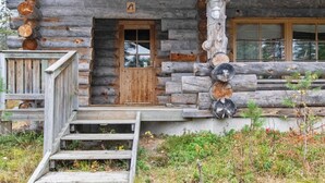 A rustic log cabin with a wooden door, a small porch, and a staircase leading to the entrance.
