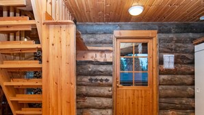 A log cabin interior with a wooden staircase, a wooden door, and a tiled floor.
