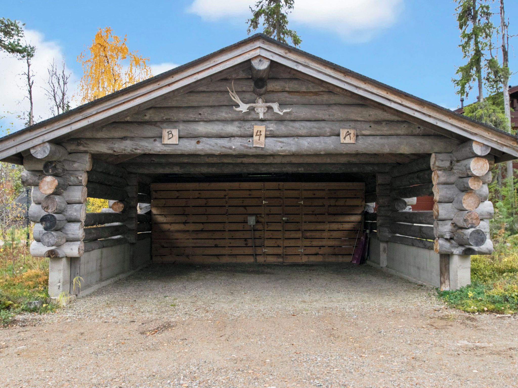 A rustic wooden building with a sloped roof, a large garage door, and a deer skull mounted above the entrance.