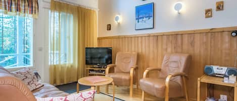Ett mysigt vardagsrum med en soffa, två fåtöljer, en tv och en träpanel på väggen.