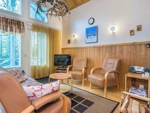 A cozy living room with a sofa, two armchairs, a television, and a wooden wall panel.