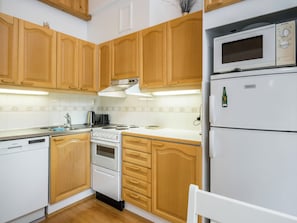 Una cocina con gabinetes de madera, lavavajillas blanco, estufa y refrigerador.