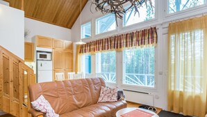 A cozy living room with a leather sofa, a small round table, and a view of a kitchen and dining area through large windows. - Isokurunpuisto a 2 by Interhome (Pelkosenniemi)